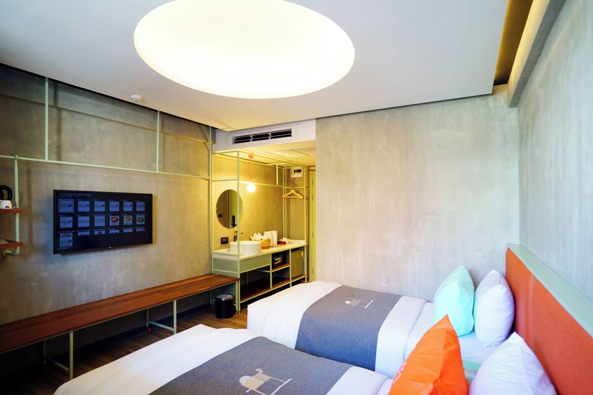 Een moderne hotelkamer met een groot bed, nachtkastjes, een bankje, een televisie en een spiegel.