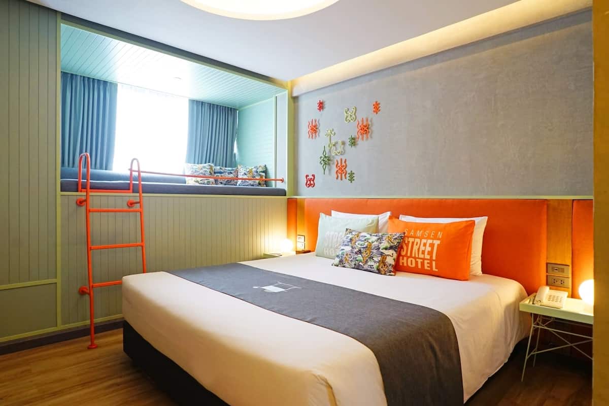 Een hotelkamer met een bed, een ladder, een nachtkastje, een telefoon en een spiegel.