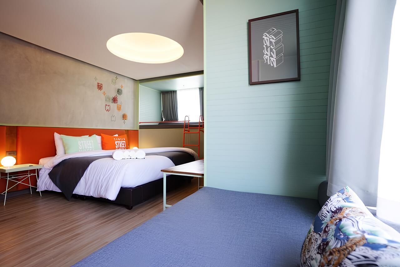 A modern hotel room with a bed, bedside table, and a small desk.
