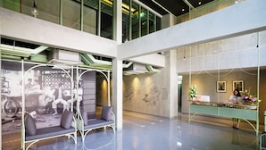 A spacious lobby with a high ceiling, a reception desk, seating area, and a wall with historical photographs.