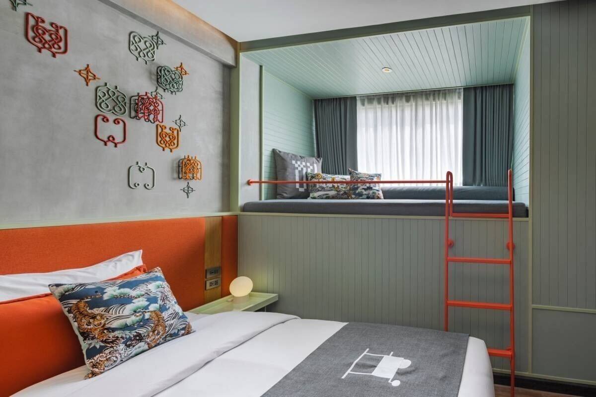 Een hotelkamer met een stapelbed, een ladder, een nachtkastje met een lamp en decoratieve wandkunst.