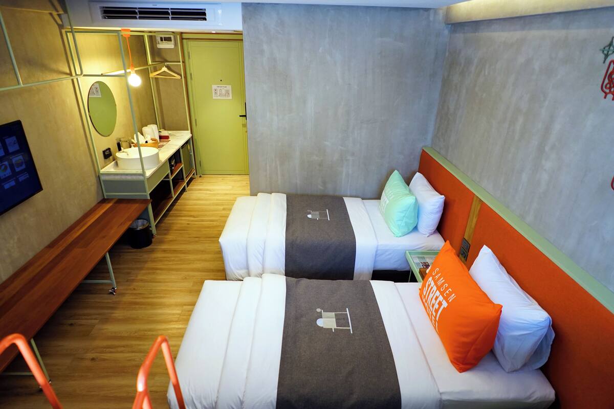 Een hotelkamer met twee bedden, een bankje, een tafeltje, een spiegel en een lamp.