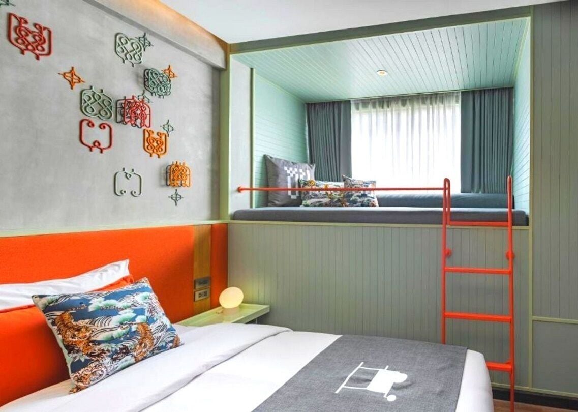 A hotel room with a bunk bed, a ladder, a wall with decorative patterns, and a window with curtains.