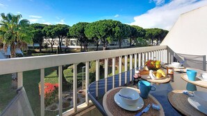 Un balcone con tavolo apparecchiato per la colazione, affacciato su un giardino con alberi e vista su edifici.
