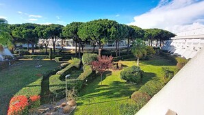 Un giardino curato con siepi ordinate, diverse specie di alberi e un edificio bianco con tetto piatto sullo sfondo.