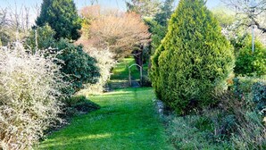A well-maintained garden path with various shrubs and trees, a clear sky, and a wooden fence in the background.