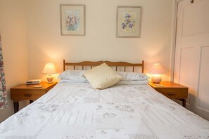 Un lit bien fait, recouvert d’une couvre-lit à motifs floraux, avec deux lampes de chevet et deux tableaux floraux encadrés accrochés au mur.