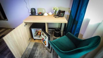 Una habitación funcional con escritorio de madera, una silla verde, un refrigerador pequeño, teléfono y cafetera.