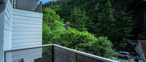 A balcony with a mesh railing overlooking a forested hillside.
