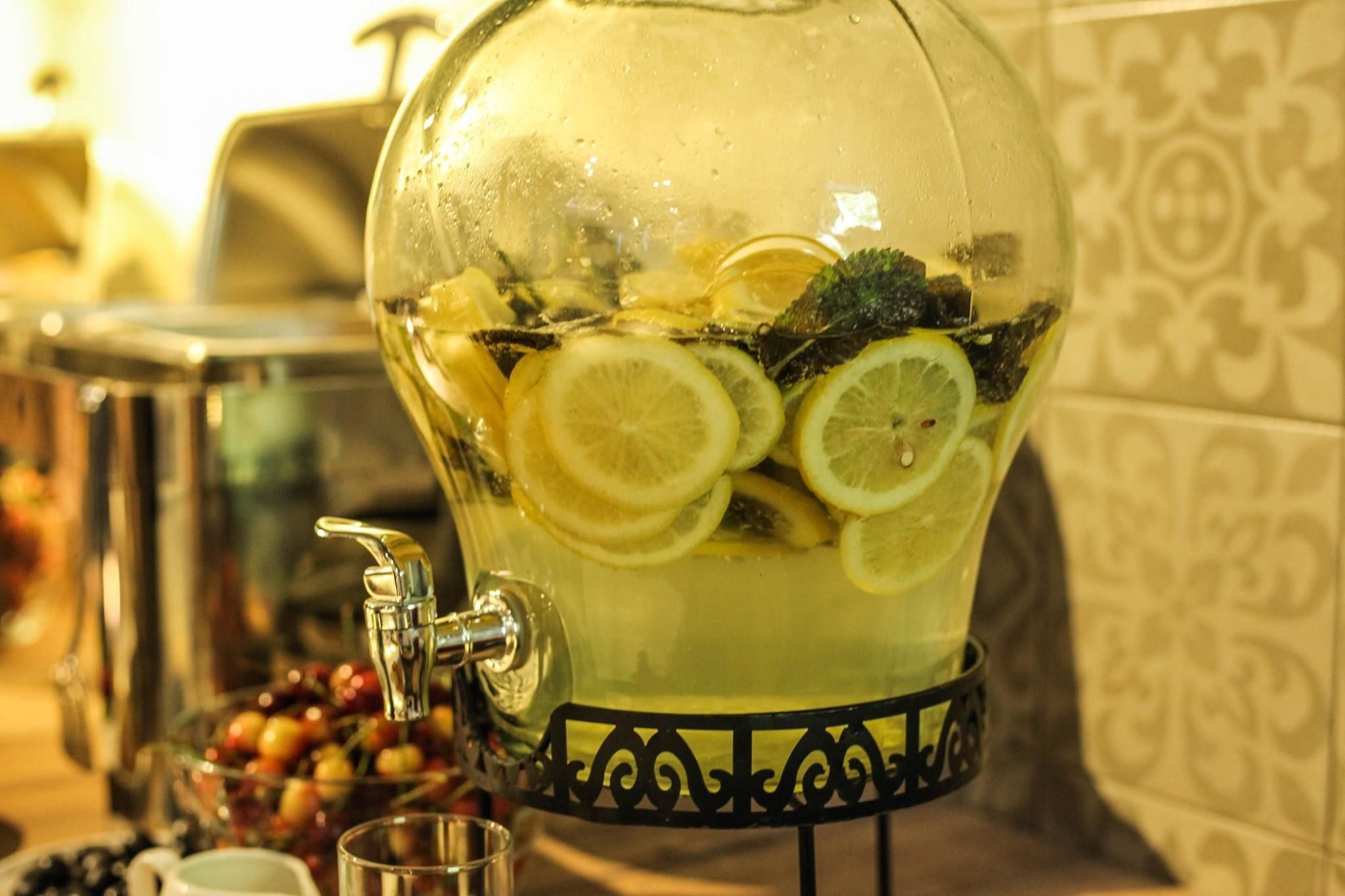 A glass punch bowl filled with a beverage and lemon slices, placed on a stand with a decorative base.