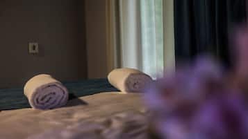 Ein Hotelzimmer mit einem Bett, zwei zusammengerollten Handtüchern, einem Fenster mit Vorhängen und einem Lichtschalter an der Wand.