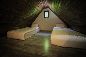 Un pequeño dormitorio en el ático con dos camas, paredes de madera, techo inclinado y una ventana pequeña.