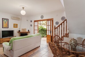 Un salon comprenant un canapé, un téléviseur, une cheminée, une table à manger avec des chaises et un escalier.