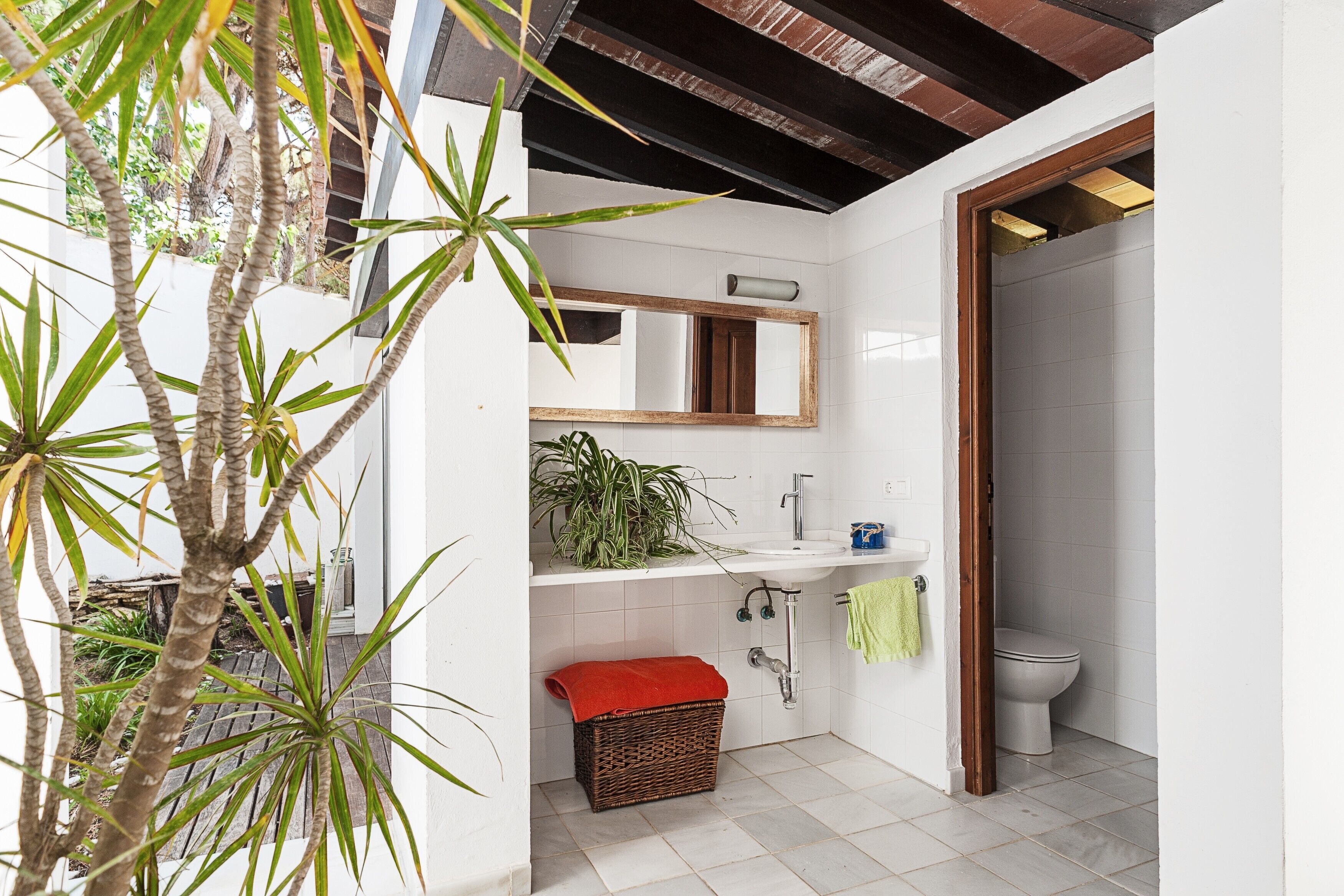A bathroom with a white sink, a mirror, a toilet, and a red towel on a basket.
