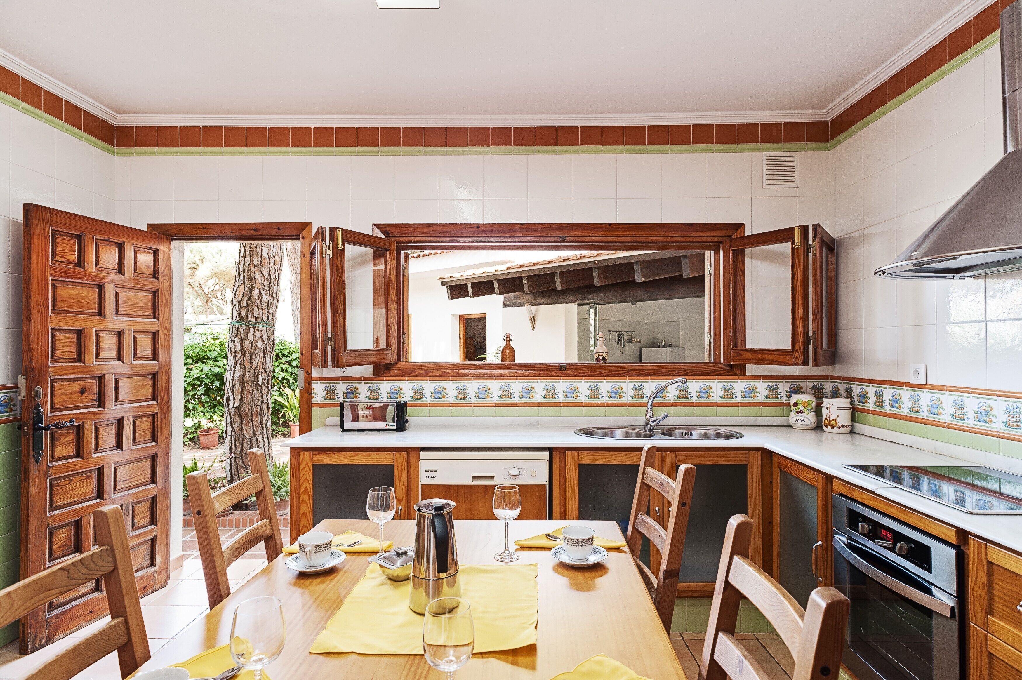 Una cocina con armarios de madera, un salpicadero de azulejos y una zona de comedor con mesa dispuesta para dos.