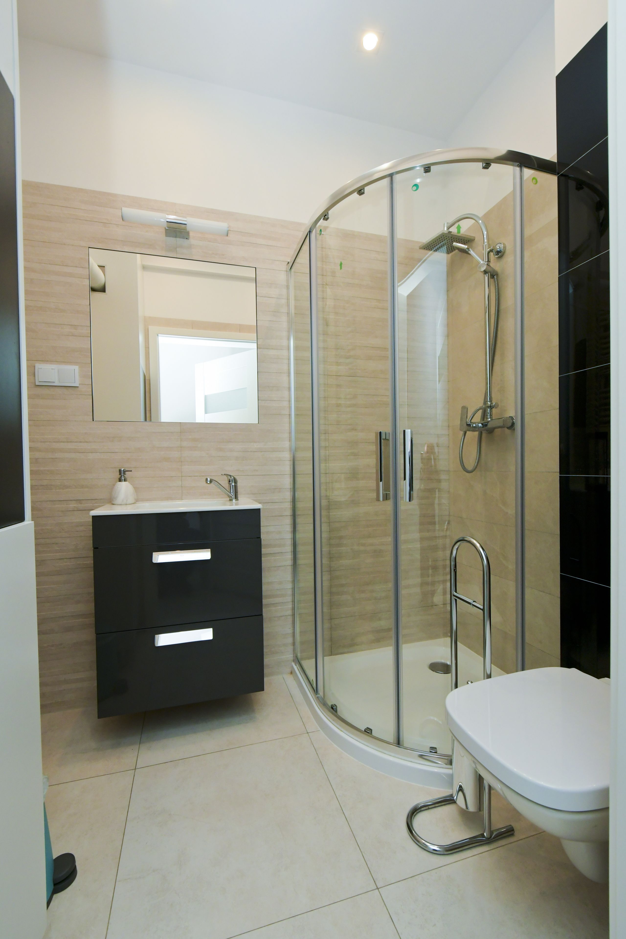 Un baño moderno con ducha de vidrio, lavamanos blanco y tocador negro.