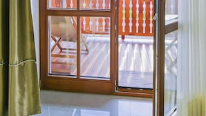 Een kamer met een grote schuifglazen deur die leidt naar een balkon met een houten terras en een rode balustrade.