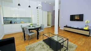 Een moderne keuken met witte kasten, een eettafel met stoelen, een glazen salontafel en een televisie aan de muur.