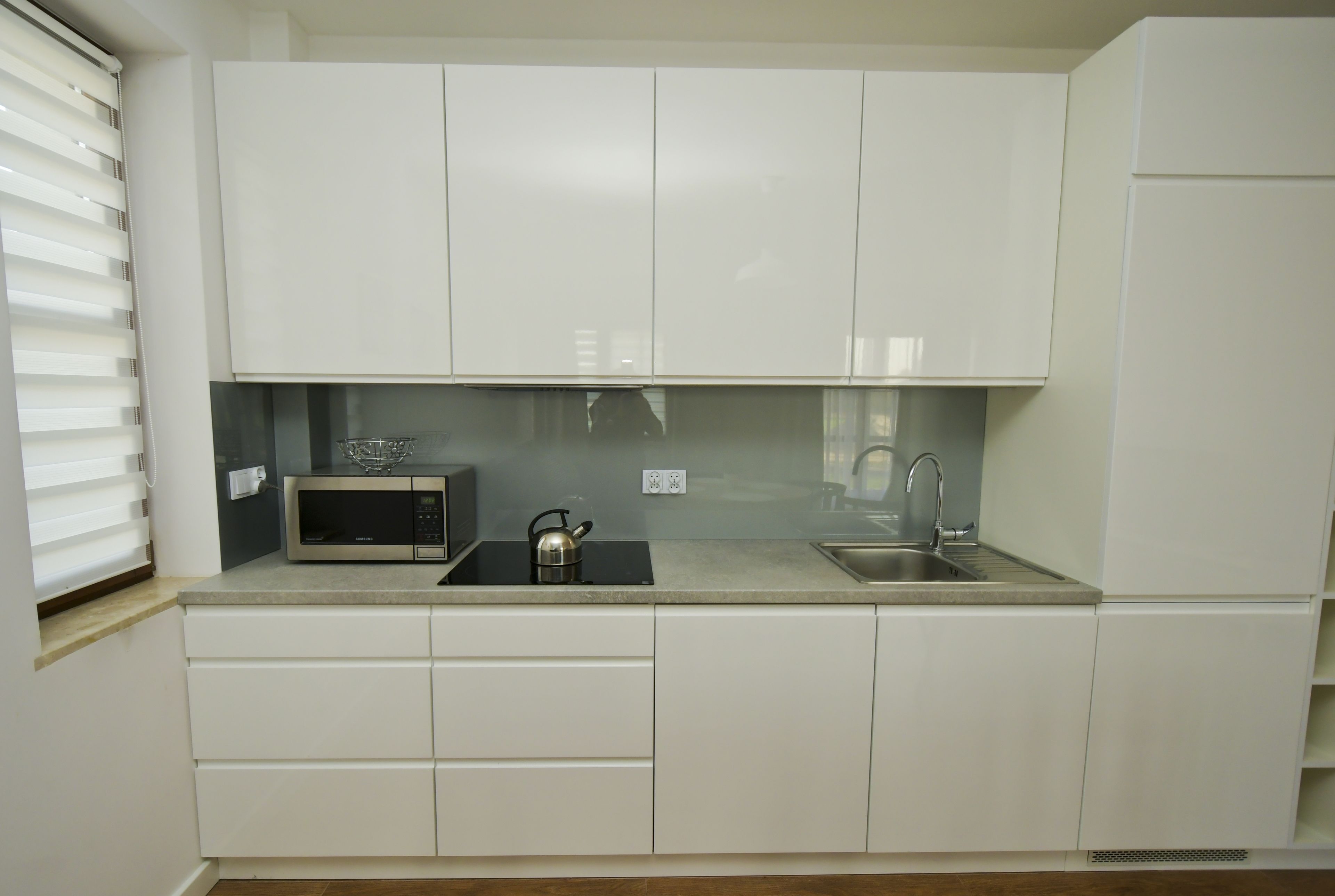 Een moderne keuken met witte kasten, een magnetron, een waterkoker en een spoelbak.