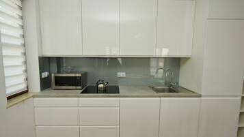 Een moderne keuken met witte kasten, een magnetron, een waterkoker en een spoelbak.