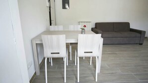 Un coin repas avec une table et quatre chaises, un canapé gris et un radiateur fixé au mur.