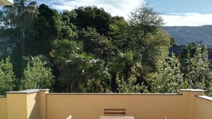 A patio with a wooden table and chairs, surrounded by a yellow wall and a view of dense trees and mountains in the background. - Apartment "G" Terrace - Levanto Cinque Terre (Levanto)
