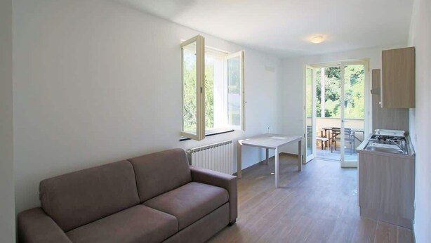 A modern living room with a sofa, a dining table, and a kitchen area with a stove. - Apartment "G" Terrace - Levanto Cinque Terre (Levanto)
