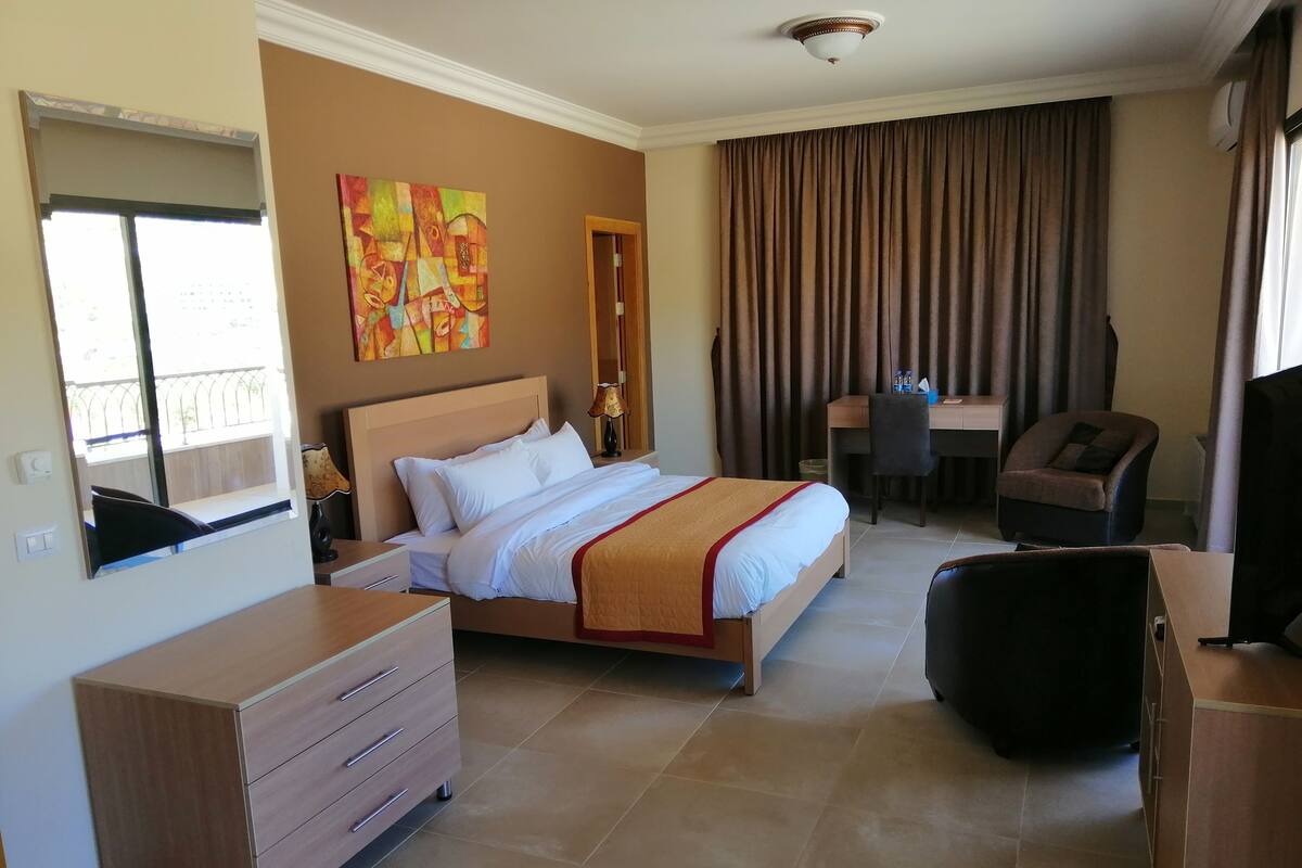 A hotel room with a bed, a desk, a chair, a dresser, and a painting on the wall.