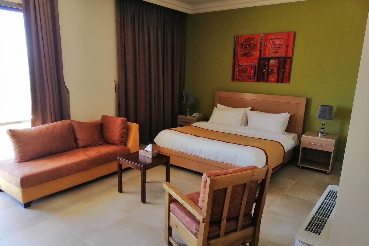 A hotel room with a bed, a sofa, a chair, a nightstand, and a lamp.