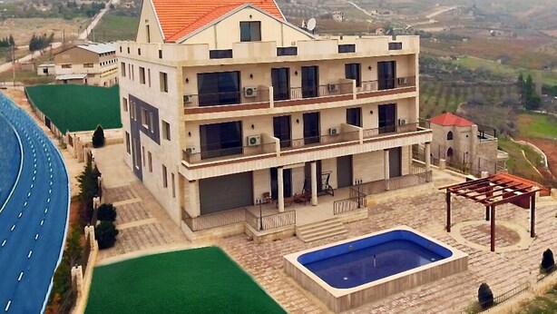 A multi-story building with a swimming pool and outdoor seating area, surrounded by a scenic landscape. - Zahle Hills Hotel (Zahlé)