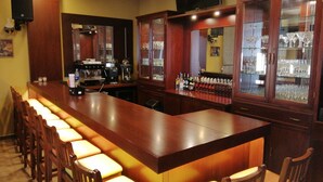 A bar area with a long counter, multiple stools, a coffee machine, and a television mounted on the wall. - Zahle Hills Hotel (Zahlé)