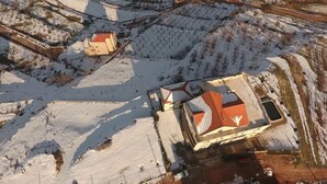 An aerial view of a building with a red roof, surrounded by snow-covered fields and a few scattered trees. - Zahle Hills Hotel (Zahlé)