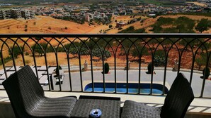 A balcony with two chairs and a small table, overlooking a town with buildings and hills in the background. - Zahle Hills Hotel (Zahlé)