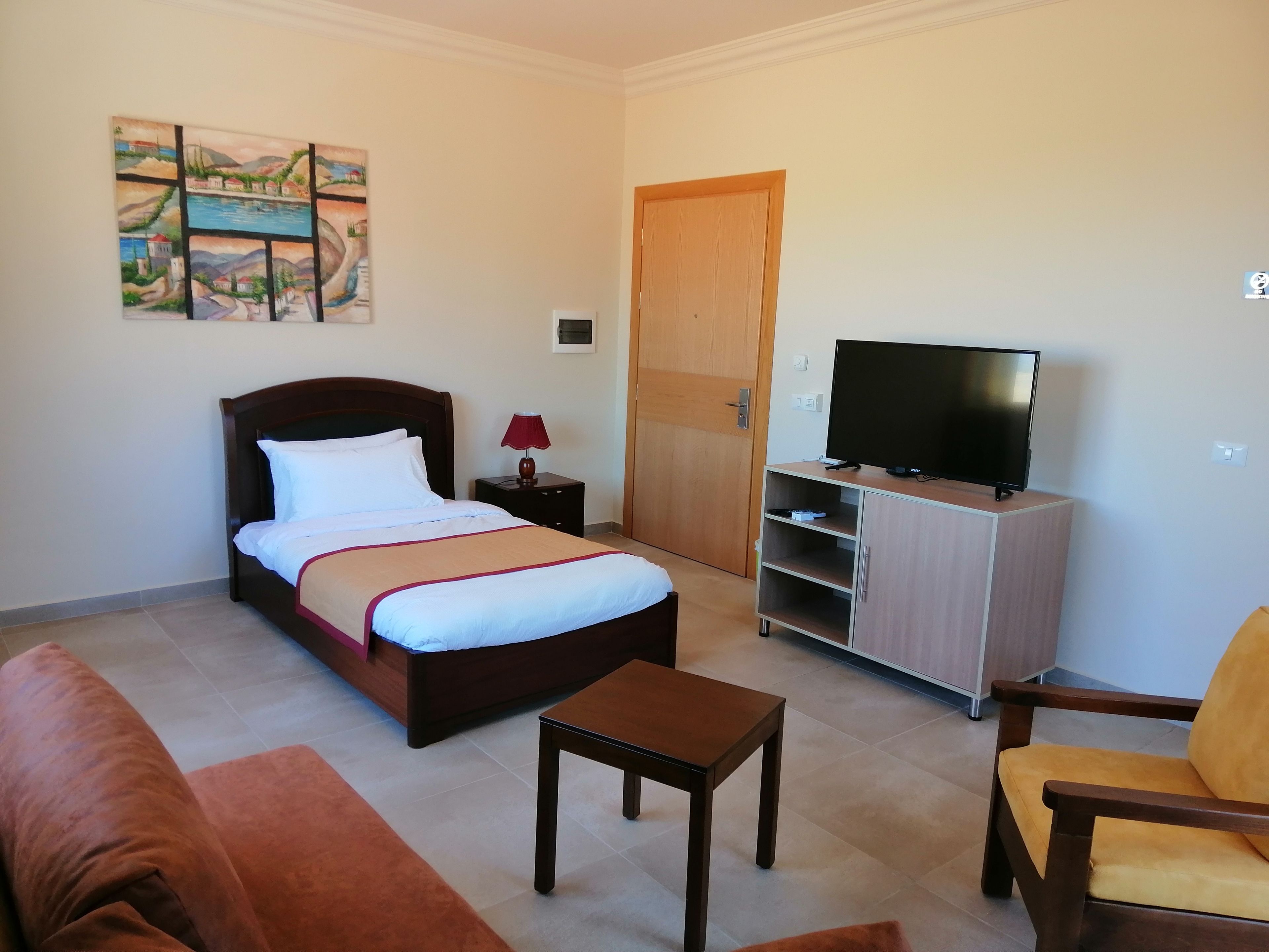 Habitación de hotel con cama, televisor en un mueble, una mesita, sofá y una puerta.