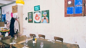 A dining area with a long wooden table set for four, chairs, and wine glasses. There are artworks on the wall and a window with a blue tint. - Regina's Banyuls - Apartment with the best view over Banyuls and the sea (Banyuls-sur-Mer)