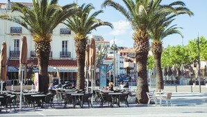 Outdoor seating with palm trees, a restaurant, and a parking sign. - Regina's Banyuls - Apartment with the best view over Banyuls and the sea (Banyuls-sur-Mer)
