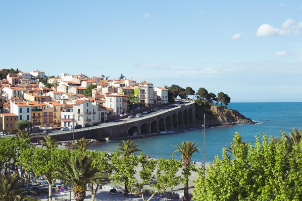 Un pueblo costero con edificios de tejados de terracota, un puente de piedra y una playa en primer plano.