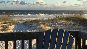 A beach with a wooden deck and a chair, overlooking the ocean with waves and clouds in the sky. - Stay right on the beach.  Enjoy the view from our updated home right on the Gulf (Gulf Shores)