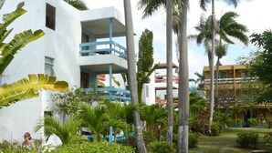 Een resort met een wit gebouw, voorzien van balkons, omgeven door weelderige begroeiing en palmbomen.