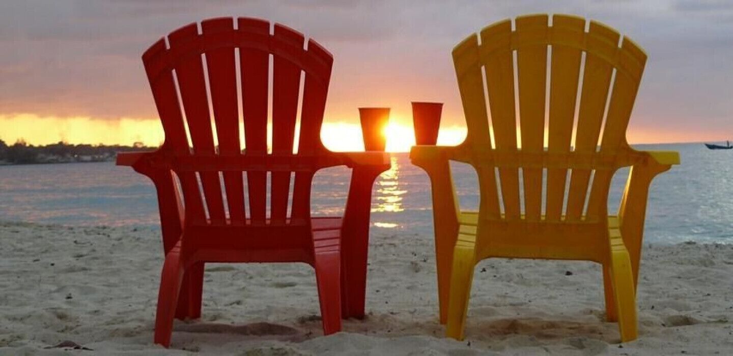Kaksi Adirondack-tyylistä puutarhatuolia, joiden edessä auringonlasku rannan yllä.
