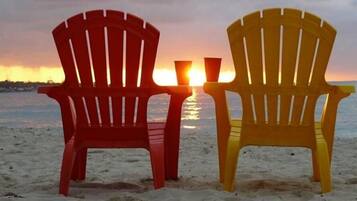Kaksi Adirondack-tyylistä puutarhatuolia, joiden edessä auringonlasku rannan yllä.