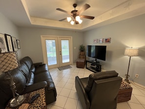 A living room with a leather couch, a flat-screen TV, a ceiling fan, and a floor lamp.