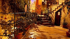 An outdoor courtyard with a stone pathway, potted plants, and a staircase leading to a building entrance. - Kaya Konak Cave Hotel (Nevsehir)