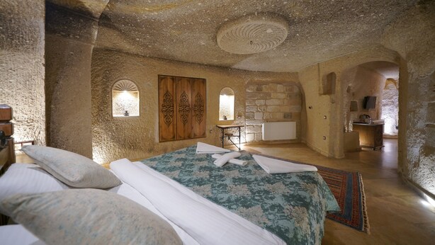 A stone-walled bedroom with a bed, a wooden wardrobe, and a small table with a lamp. - Kaya Konak Cave Hotel (Nevsehir)