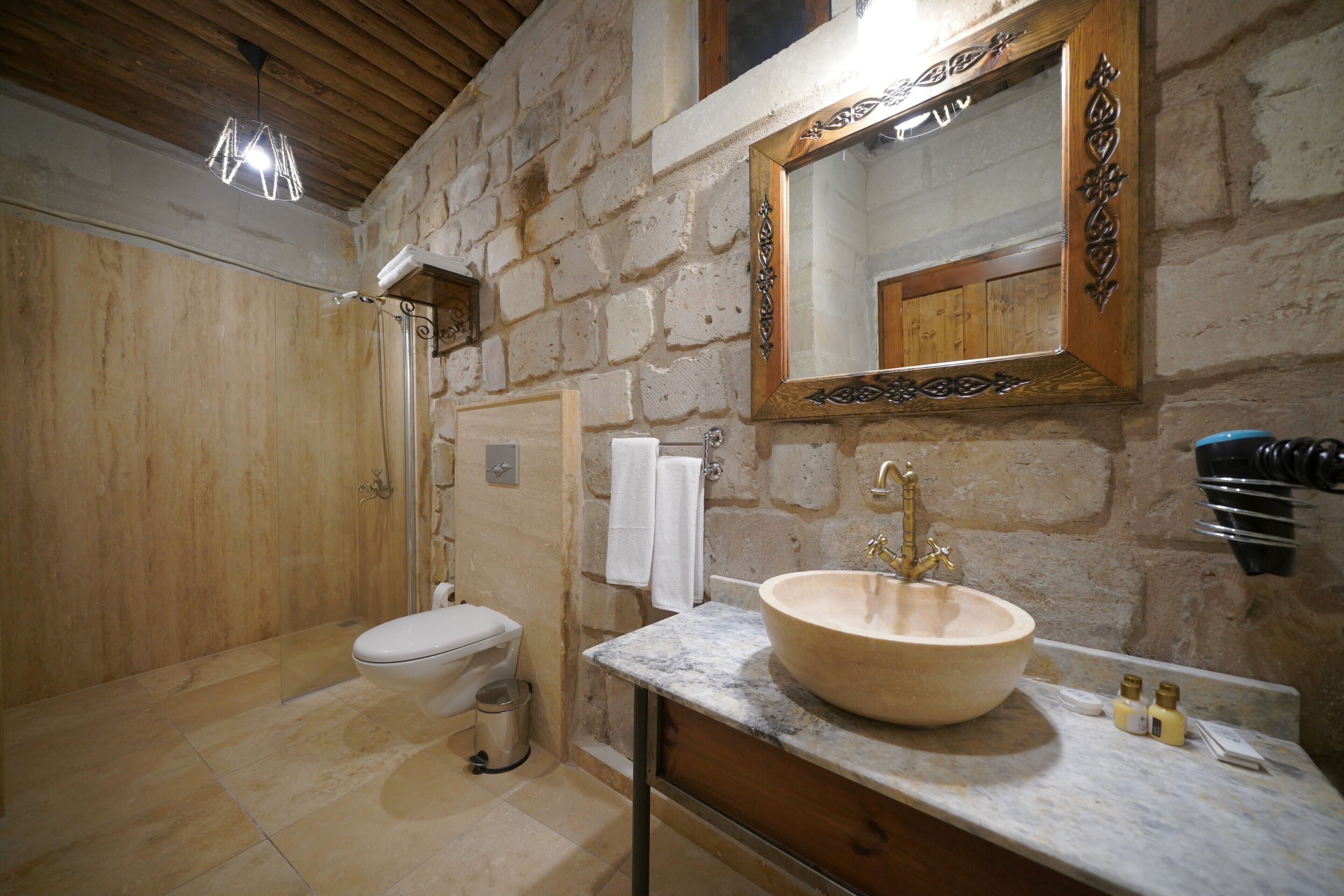Un bagno con parete in pietra, soffitto in legno, lavabo in marmo e specchio con cornice in legno.
