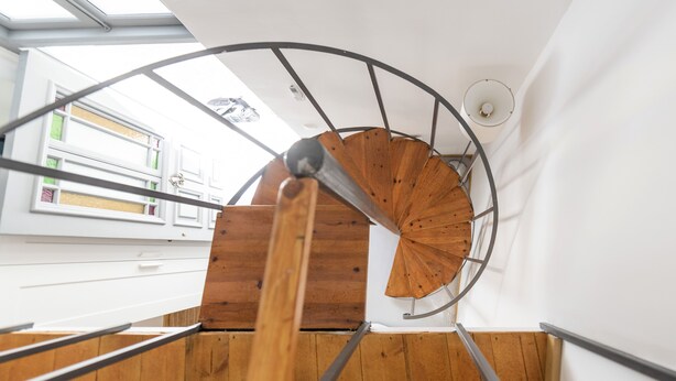 Una escalera de caracol con peldaños de madera y barandillas de metal, que sube a un nivel superior.