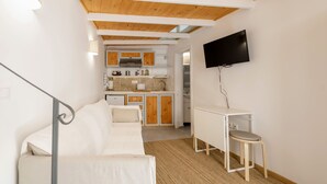 Un espacio habitable compacto con kitchenette, un sofá, una mesita y un televisor montado en la pared.