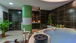 Ein modernes Badezimmer mit einer großen Badewanne, einer grünen Mosaiksäule und dunkel gefliesten Wänden.