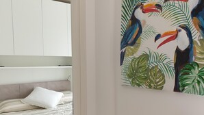 Ein Schlafzimmer mit einem Bett, eine weiße Kommode, einem Wandbild mit Tukanen und einer kleinen Ablage mit Dekoration.