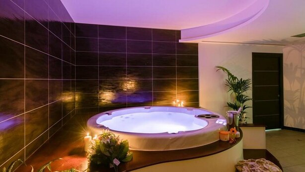 Ein moderner Wellnessraum mit Whirlpool, dunklen Fliesenwänden und stimmungsvoller Beleuchtung.